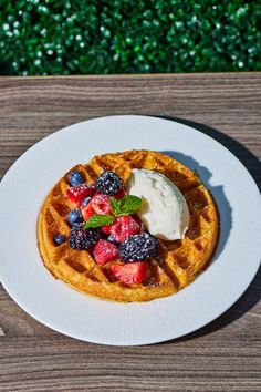 a waffle topped with fruit and ice cream on a white plate sitting on a wooden table