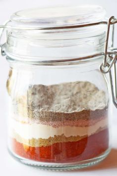 a jar filled with different colored food on top of a white table next to a spoon