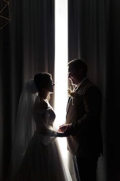 a bride and groom are standing in front of the light coming through the curtains at their wedding