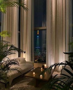 a living room filled with furniture and lots of windows next to tall buildings at night