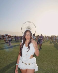 a woman standing on top of a lush green field next to a carnival ferris wheel