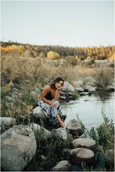 a woman sitting on rocks next to a river