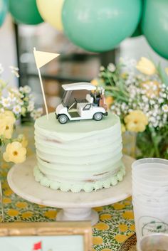 a small car is on top of a white cake with green frosting and yellow flowers