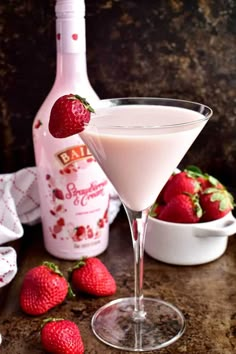 a martini glass filled with liquid and strawberries next to a bottle of booze