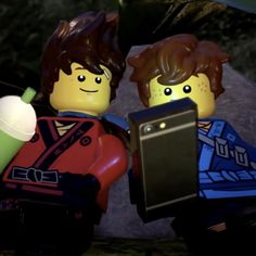 two legos are standing next to each other and one is holding a cell phone