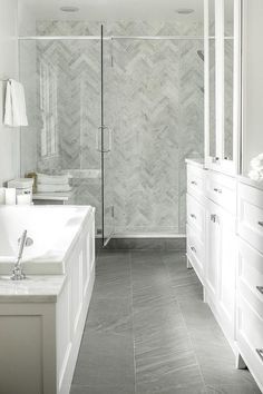 a bathroom with white cabinets and gray tile flooring, along with a walk in shower