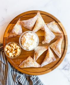 a wooden plate topped with pastries next to a bowl of whipped cream