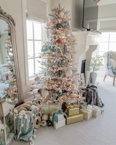 a decorated christmas tree in a living room next to a mirror and fireplace with presents on the floor