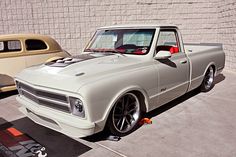 an old pick up truck parked in front of a wall next to a classic car