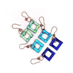 three pieces of blue and green glass are hanging from copper earwires on white background