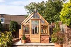 a small wooden greenhouse in the middle of a brick garden area with potted plants