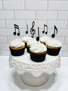 four cupcakes with white frosting and music notes on top are sitting on a cake stand