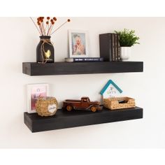 two black floating shelves with pictures and toys on them, one shelf has a toy truck