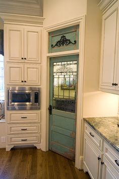 a kitchen with white cabinets and wood flooring next to an open door that leads to a window