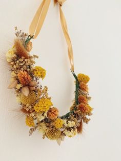 a wreath made out of dried flowers and leaves hanging on a wall with a ribbon