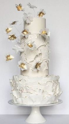 a three tiered cake with white frosting and gold flowers on the top layer