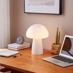 a laptop computer sitting on top of a wooden desk next to a mushroom shaped lamp