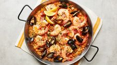 a pan filled with seafood and rice on top of a yellow striped table cloth next to a lemon wedge