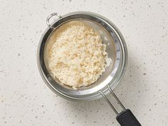 a metal bowl filled with rice on top of a white counter next to a black spatula