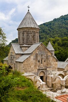 an old church in the middle of a forest with mountains in the backgroud