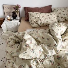 an unmade bed with floral comforter and pillows on the floor next to a table