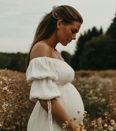 a pregnant woman standing in a field of flowers with her hands on her belly and looking down