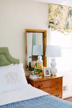 a bedroom with a bed, dresser and mirror in the corner next to a window