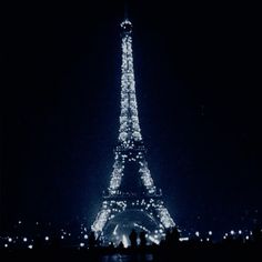 the eiffel tower lit up at night with people standing in front of it