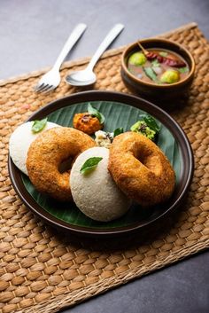 some food is sitting on a plate next to a bowl and silverware with spoons