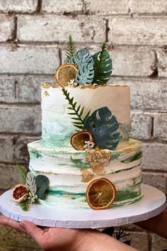 a hand holding a multi layer cake decorated with leaves and oranges