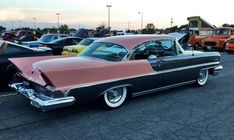 an old pink and black car parked in a parking lot next to other classic cars