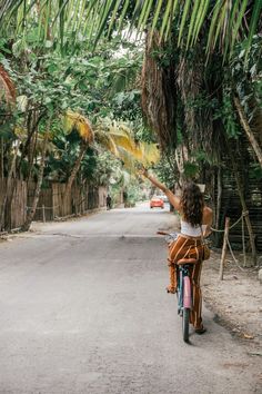 a woman riding a bike down a street next to palm trees