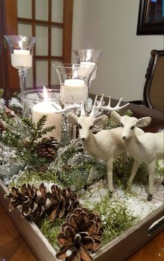 two white deer figurines sitting on top of a tray filled with pine cones