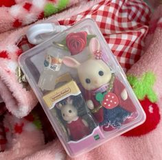 a couple of small toy animals in a plastic container on a pink blanket with red and white checkered pillows