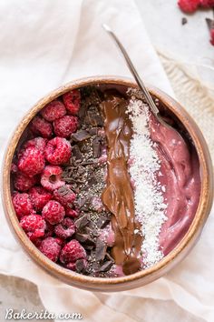 a bowl filled with chocolate and raspberries on top of a white cloth next to a spoon