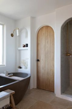 a bath tub sitting next to a wooden door in a white bathroom with a large window