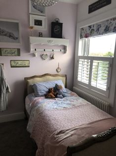 a small child's bedroom with pink walls and white shuttered windows, teddy bear on the bed