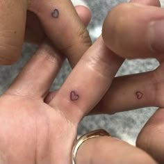 two people holding hands with small hearts tattooed on their thumbnails and finger rings