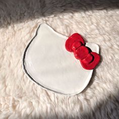 a white plate with a red hello kitty decoration on it's side sitting on a fluffy surface