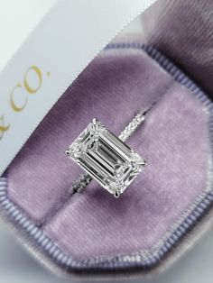 an emerald - cut diamond ring sits in its velvet case