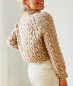 a woman wearing a sweater and white pants is smiling at the camera with her hands on her hips