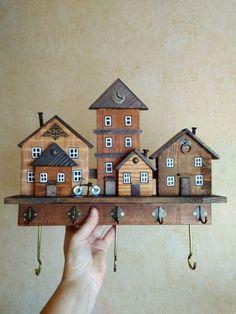 a person is holding up a shelf with several wooden houses on it and hooks hanging from the wall