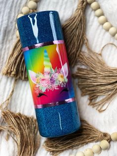 a blue glitter tumbler with unicorns and flowers on it sitting next to tassels