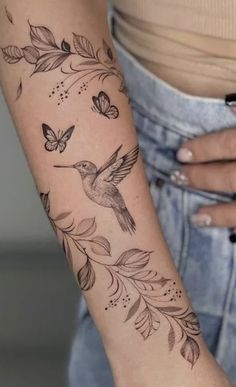 a woman's arm with a hummingbird and leaves tattoo on the left forearm