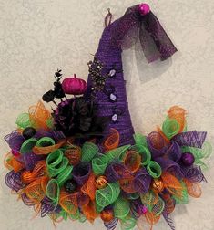 a purple witch hat with green and orange mesh decorations on the front, hanging from a wall