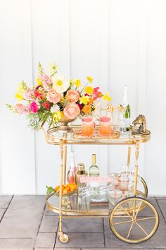 a gold bar cart with flowers and drinks on it for a brunch or cocktail party