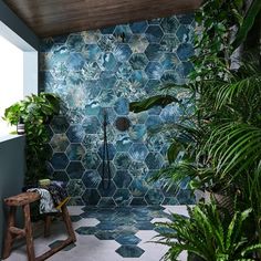 a bathroom with blue tiled walls and plants in the corner, along with a wooden bench