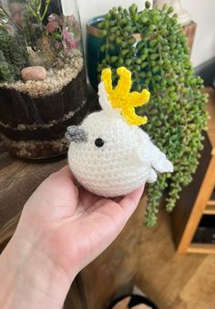 a hand holding a small crocheted bird with a yellow flower on it's head