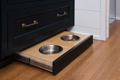 two stainless steel bowls are in the bottom drawer of a black cabinet next to a wooden floor