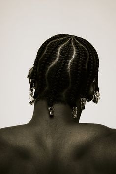 the back of a woman's head with braids and earrings on her neck